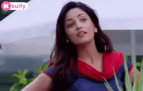 A Woman In A Blue And Red Dress Is Standing In Front Of A White Tent And Looking At The Camera . GIF