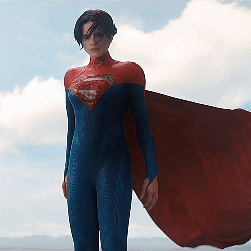 A Woman In A Blue And Red Superman Costume Stands In Front Of A Cloudy Sky GIF