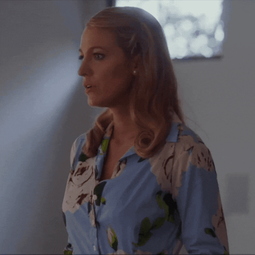 a woman in a blue and white floral shirt is standing in front of a window