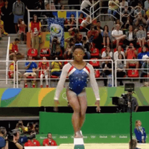 A Woman In A Blue And White Leotard Is Balancing On A Balance Beam In Front Of A Crowd GIF