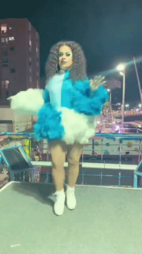 A Woman In A Blue And White Outfit Is Standing On A Stage GIF