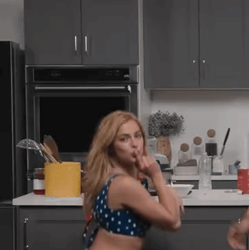 A Woman In A Blue And White Polka Dot Top Stands In A Kitchen GIF