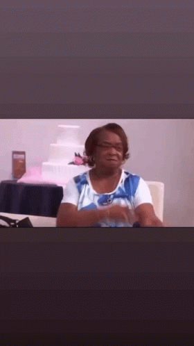 A Woman In A Blue And White Shirt Is Sitting At A Table In Front Of A Wedding Cake . GIF