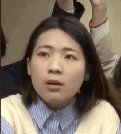 A Woman In A Blue And White Striped Shirt Is Making A Funny Face While Sitting In A Crowd . GIF