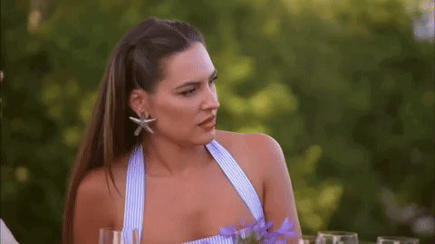 A Woman In A Blue And White Striped Top Is Sitting At A Table With Wine Glasses . GIF