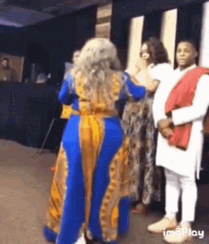 a woman in a blue and yellow dress is dancing in front of a crowd of people .