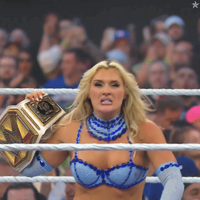 A Woman In A Blue Bra And Blue Gloves Is Holding A Wrestling Belt GIF