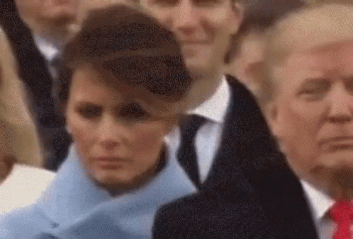 A Woman In A Blue Coat And A Man In A Suit Are Standing In A Crowd Of People . GIF