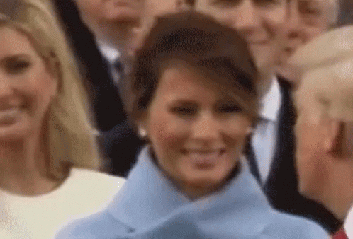 A Woman In A Blue Coat Is Smiling In Front Of A Crowd . GIF
