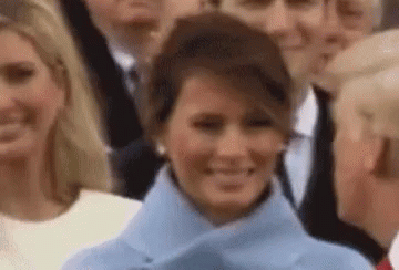 A Woman In A Blue Coat Is Smiling In Front Of A Crowd . GIF