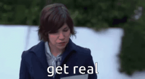 A Woman In A Blue Coat Is Standing In The Snow And Says Get Real GIF