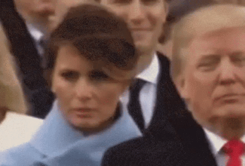 A Woman In A Blue Coat Is Standing Next To A Man In A Suit And Tie Giving A Thumbs Up . GIF