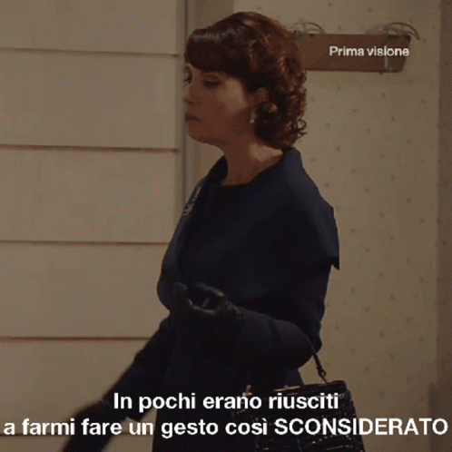 A Woman In A Blue Coat Stands In Front Of A Sign That Says Prima Visione GIF