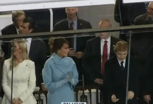 A Woman In A Blue Coat Stands In Front Of A Sign That Says ' Talking ' On It GIF