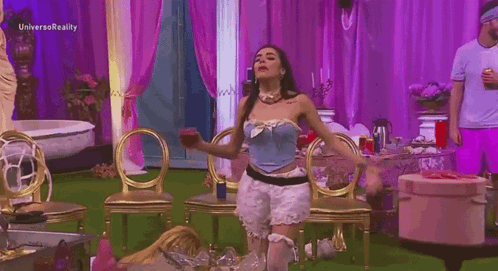 a woman in a blue corset is dancing in a room with purple curtains and gold chairs .