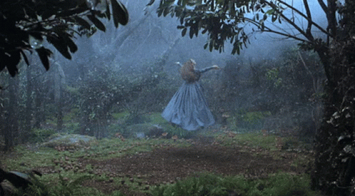 A Woman In A Blue Dress Is Dancing In A Dark Forest GIF