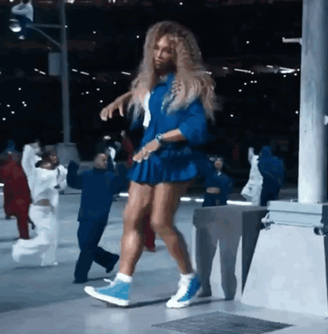 A Woman In A Blue Dress Is Dancing In Front Of A Group Of People GIF