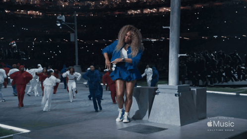 a woman in a blue dress is dancing in front of a music halftime show banner