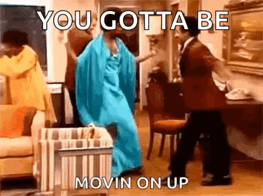 A Woman In A Blue Dress Is Dancing With A Man In A Suit In A Living Room . GIF