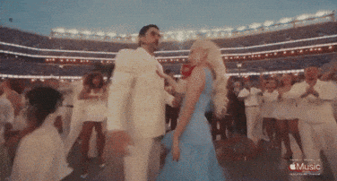 A Woman In A Blue Dress Is Dancing With A Man In A White Suit In A Stadium With The Words Music On The Bottom GIF