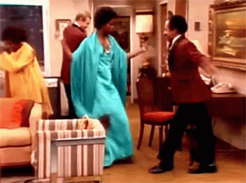A Woman In A Blue Dress Is Dancing With Two Men In A Living Room . GIF