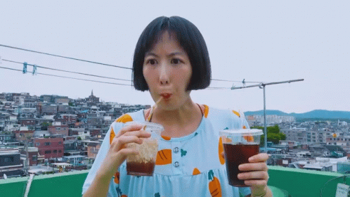 A Woman In A Blue Dress Is Drinking From A Plastic Cup GIF