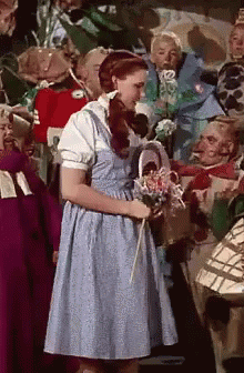 A Woman In A Blue Dress Is Holding A Basket Of Flowers GIF