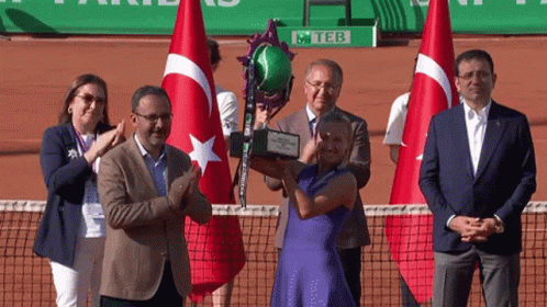 A Woman In A Blue Dress Is Holding A Trophy In Front Of A Sign That Says Teb GIF