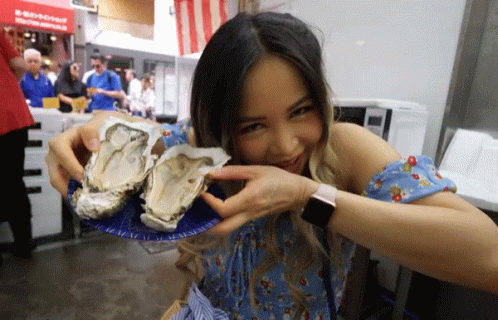 A Woman In A Blue Dress Is Holding Two Oysters On A Plate GIF