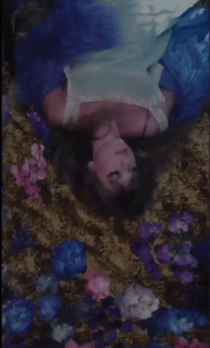 A Woman In A Blue Dress Is Laying In A Bed Of Flowers . GIF