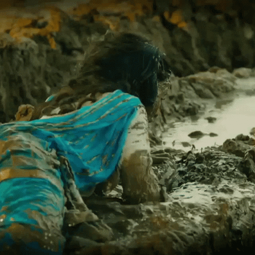 A Woman In A Blue Dress Is Laying In The Mud On The Beach GIF