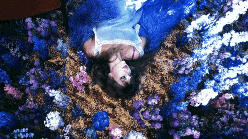 A Woman In A Blue Dress Is Laying On Her Back In A Field Of Blue Flowers GIF