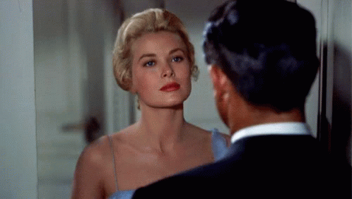 A Woman In A Blue Dress Is Looking At Herself In A Mirror While A Man In A Suit Looks On . GIF