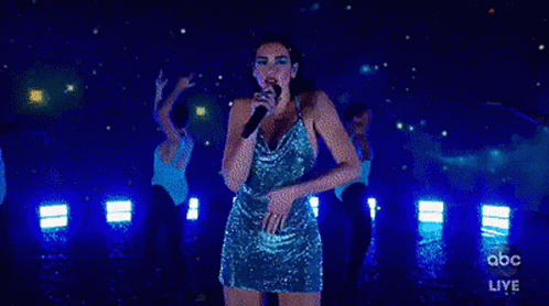 A Woman In A Blue Dress Is Singing Into A Microphone On Stage . GIF