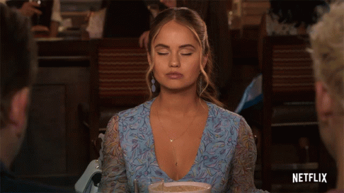 A Woman In A Blue Dress Is Sitting At A Table With A Netflix Logo In The Corner GIF