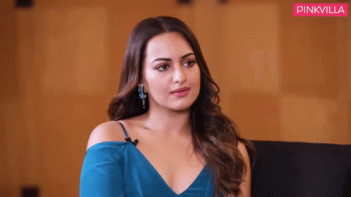 A Woman In A Blue Dress Is Sitting In Front Of A Pink Villa Banner GIF