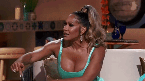 A Woman In A Blue Dress Is Sitting On A Couch With Her Hands On Her Knees . GIF