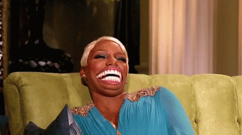 A Woman In A Blue Dress Is Sitting On A Green Couch And Laughing . GIF