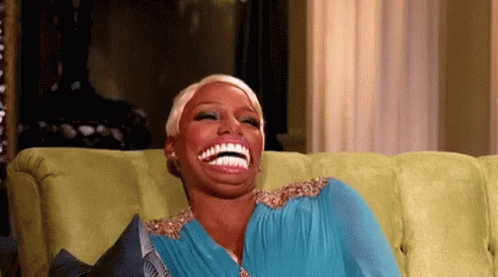 a woman in a blue dress is sitting on a green couch and laughing .