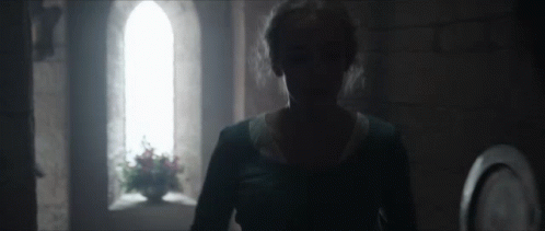 A Woman In A Blue Dress Is Standing In A Dark Room In Front Of A Window . GIF