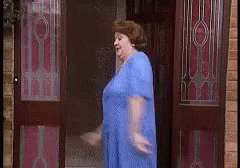 A Woman In A Blue Dress Is Standing In A Doorway GIF
