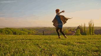 A Woman In A Blue Dress Is Standing In A Grassy Field With Her Arms Outstretched GIF