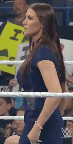A Woman In A Blue Dress Is Standing In A Wrestling Ring In Front Of A Crowd . GIF
