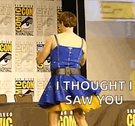 A Woman In A Blue Dress Is Standing In Front Of A Comic Con Sign . GIF