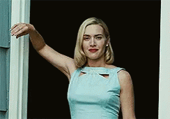 A Woman In A Blue Dress Is Standing In Front Of A Door . GIF