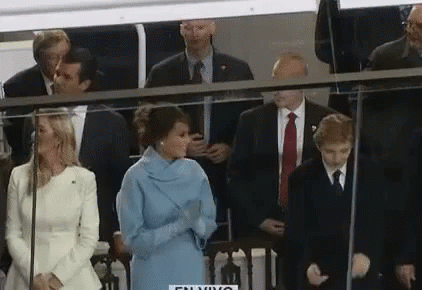 A Woman In A Blue Dress Is Standing In Front Of A Group Of People In Suits And Ties . GIF
