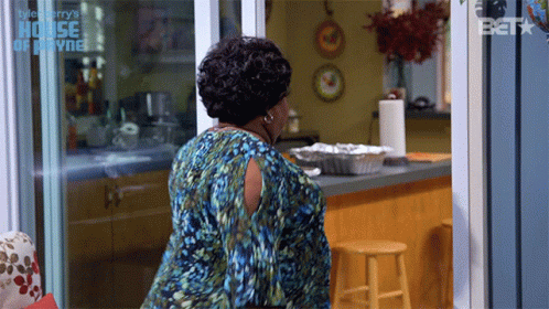 A Woman In A Blue Dress Is Standing In Front Of A Sliding Glass Door That Says House Of Payne GIF