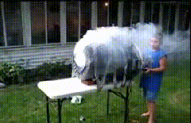 A Woman In A Blue Dress Is Standing In Front Of A Table With Smoke Coming Out Of It GIF