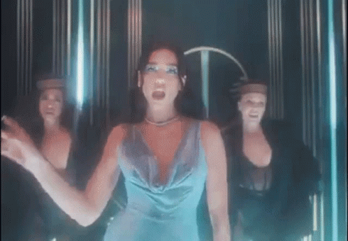 A Woman In A Blue Dress Is Standing In Front Of Three Dancers In A Dark Room . GIF