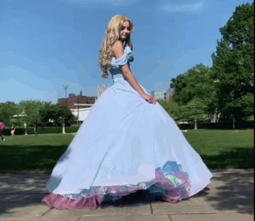 A Woman In A Blue Dress Is Standing On A Sidewalk GIF